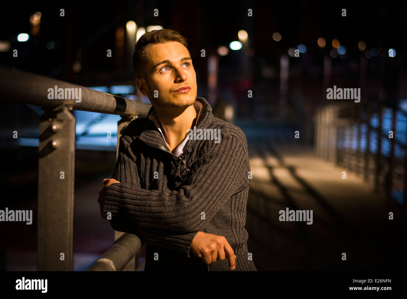 Handsome blond young man alone in urban setting, leaning against handrail, night shot Stock Photo
