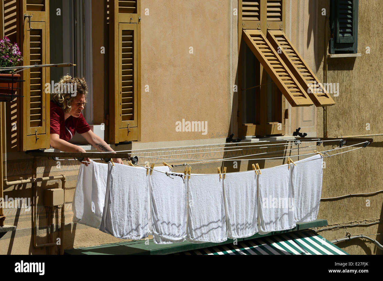Woman hanging washing on line from window Riomaggiore on the Cinque Terre in Italy / drying nappies mother Stock Photo