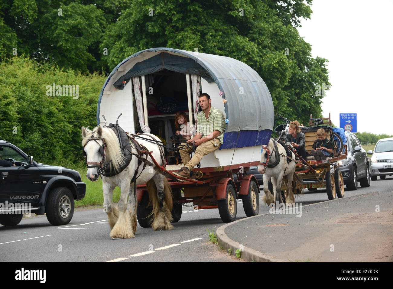 Travellers in bow top horse drawn caravan travelling along busy road in West Midlands Uk / travellers wagon gypsy romany Stock Photo