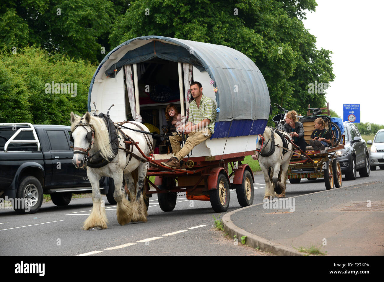 Travellers in bow top horse drawn caravan travelling along busy road in West Midlands Uk / travellers wagon gypsy romany Stock Photo