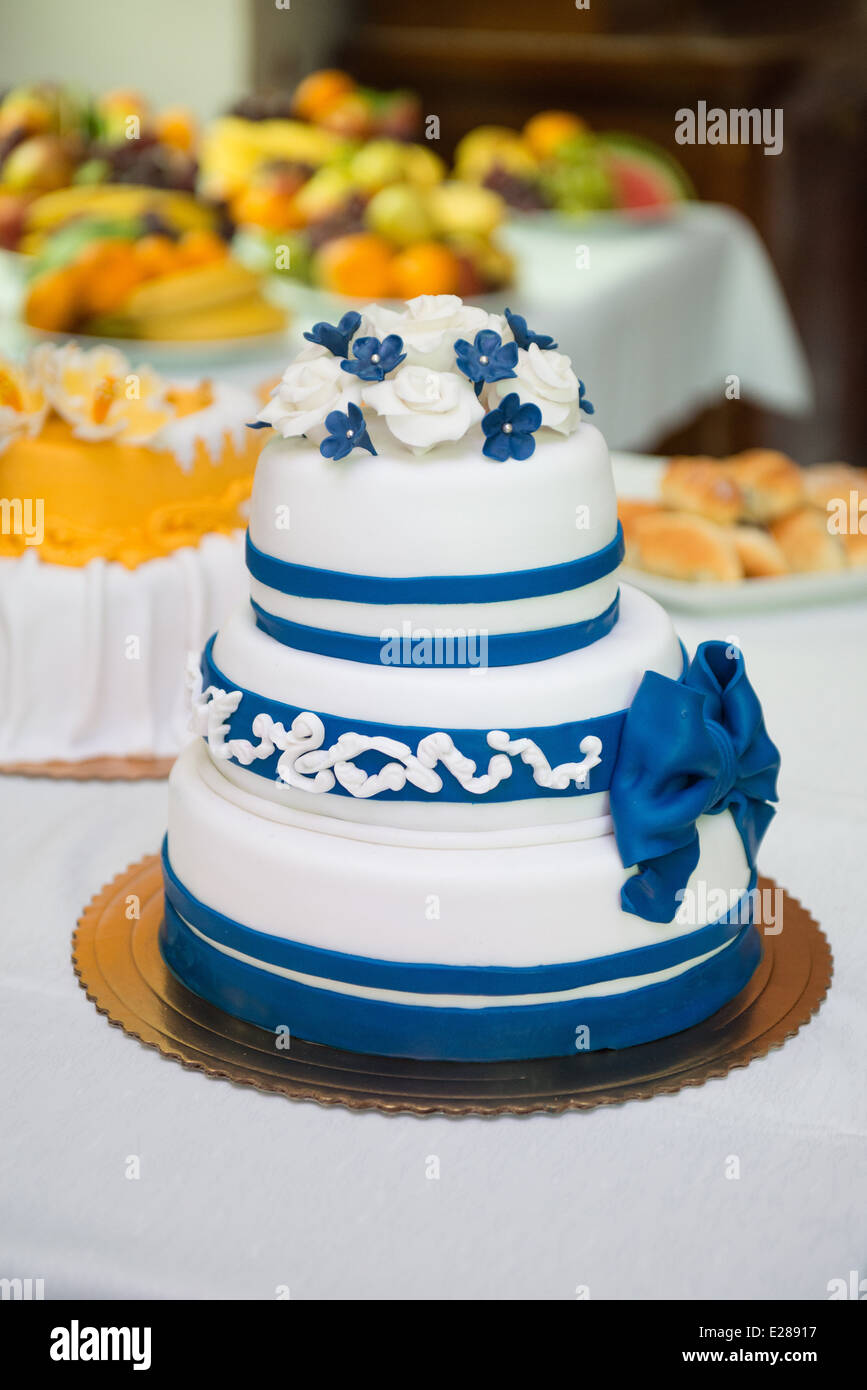 Delicious wedding cake in blue and white color combination, selection of various fruits in background Stock Photo
