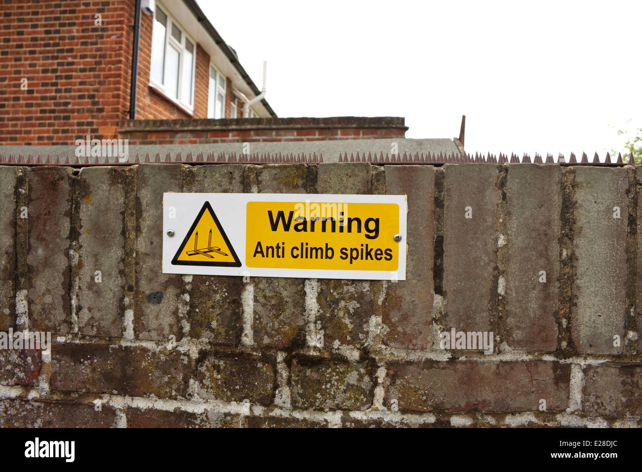 A garden wall backing on to a public highway with anti-climb spikes on top with a warning sign Stock Photo