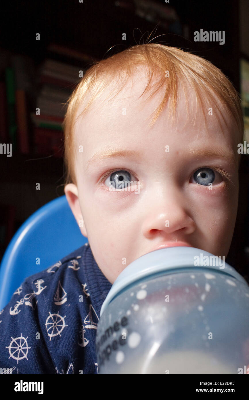 Fair haired caucasian baby looking tired and drinking milk from a bottle Stock Photo