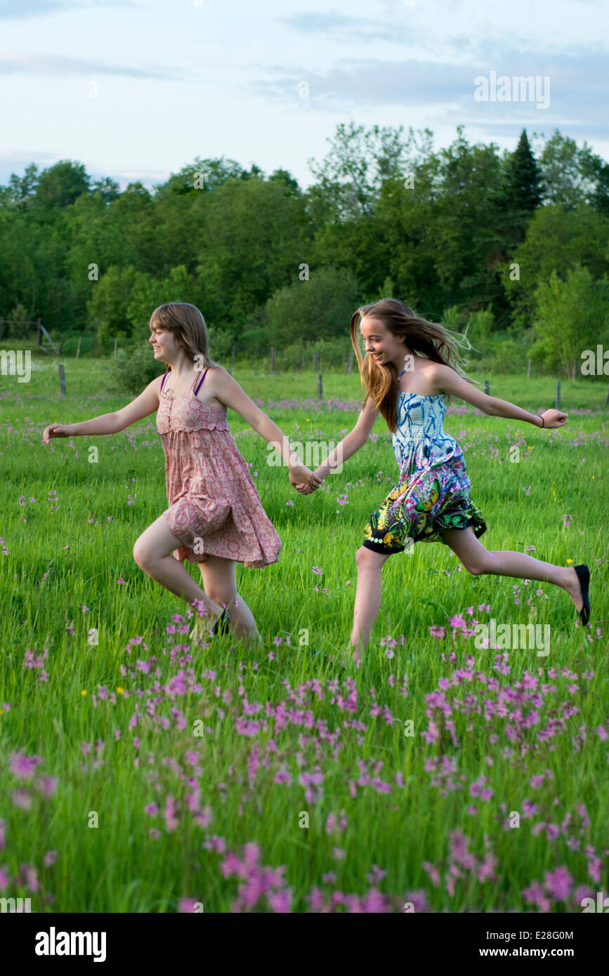 Two teenage girls running in a field of flower at sunset. Real friends in real life, they