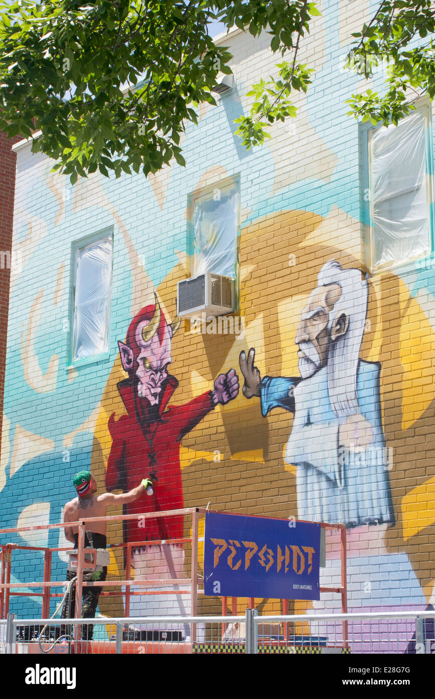 A graffiti artist spray paints a wall on the Plateau Mont-Royal during the Montreal Mural Festival Stock Photo
