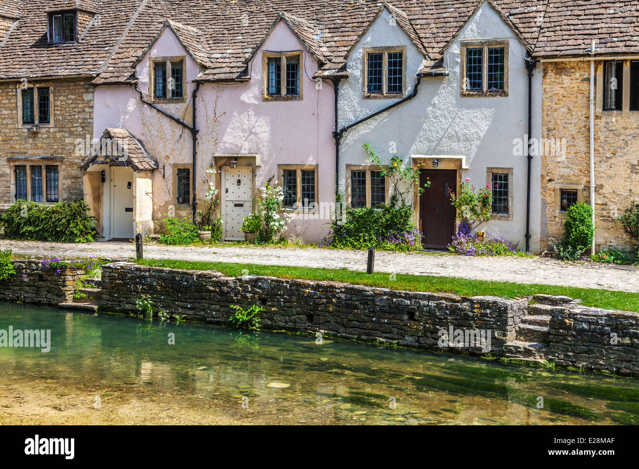 A row of pretty terraced cottages alongside the river Bybrook in the Cotswold village of Castle Combe in Wiltshire. Stock Photo