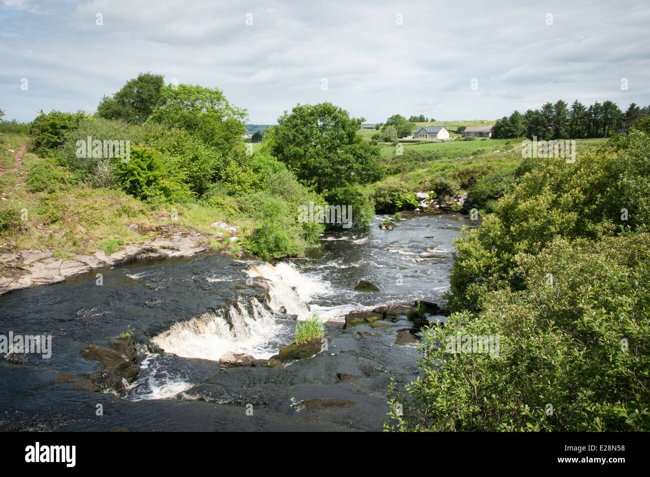 River with waterfall runs through green Irish countryside Stock Photo