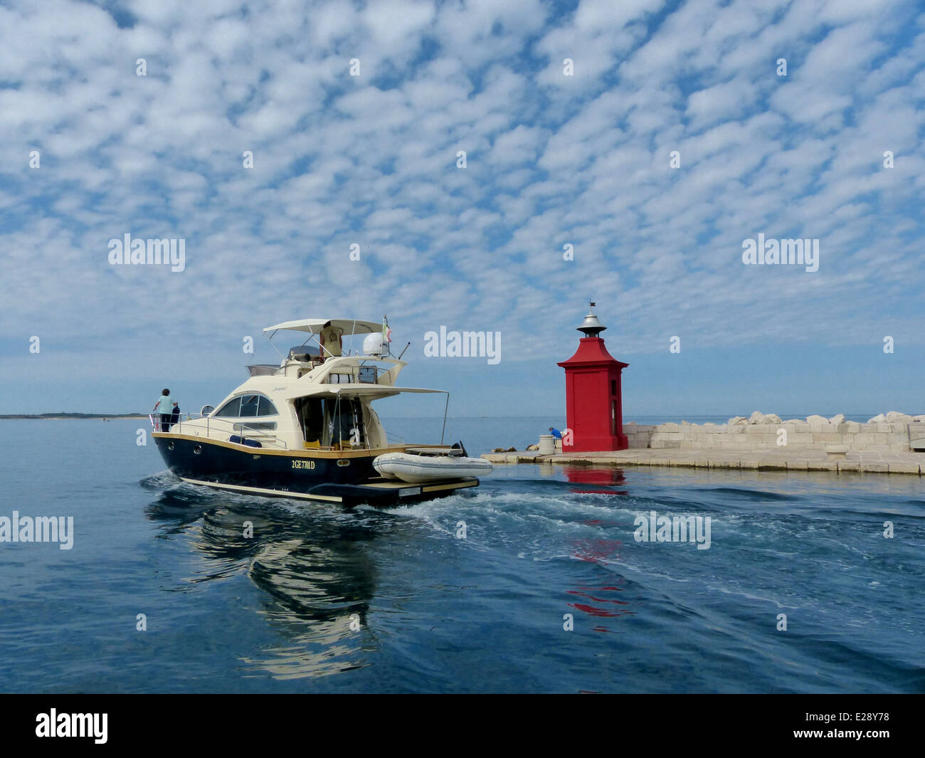 A motor yacht sailing out of harbour past a red post in Piran, Slovenia Stock Photo