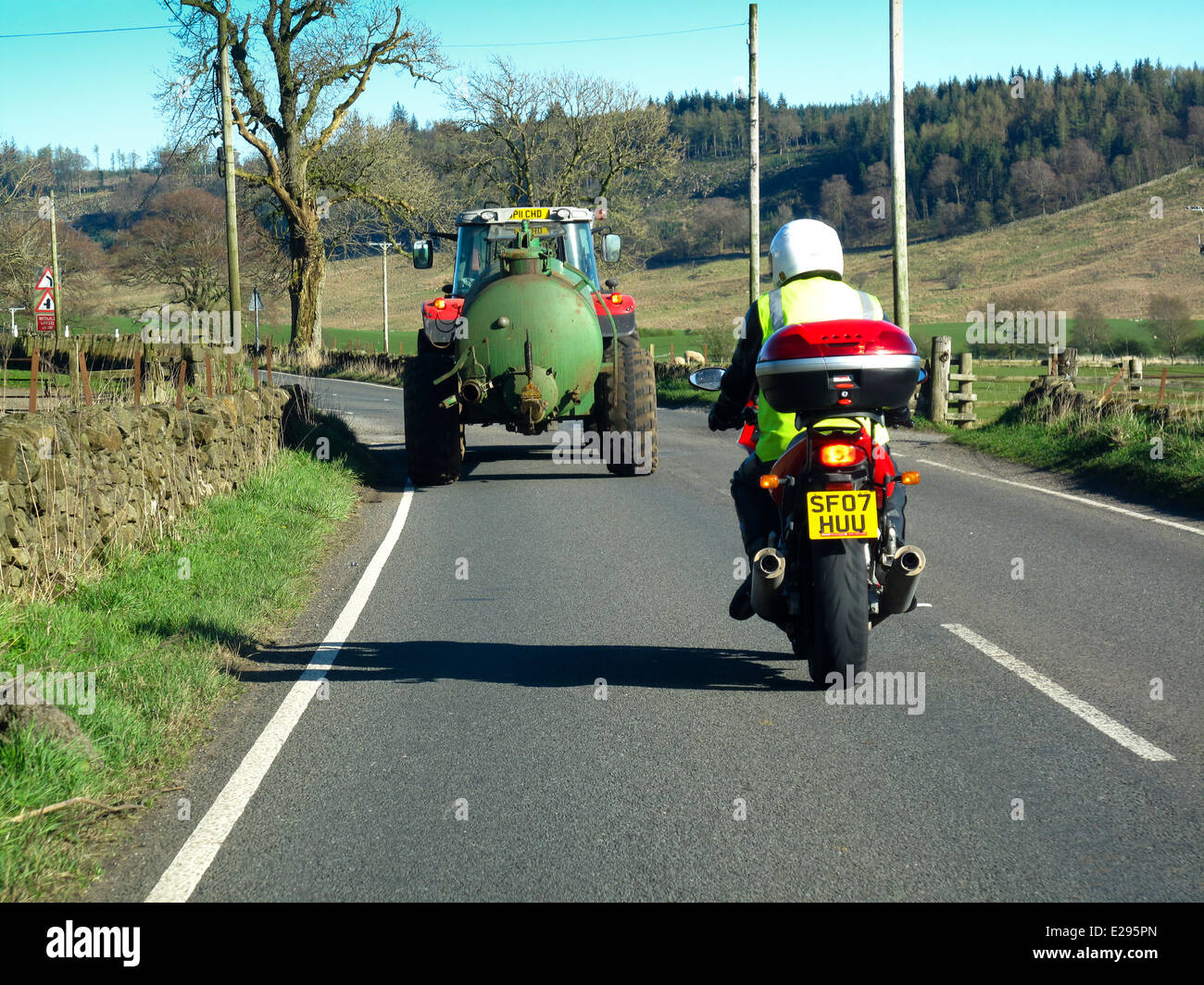 Motorbike following tractor and trailer tank on rural road Stock Photo