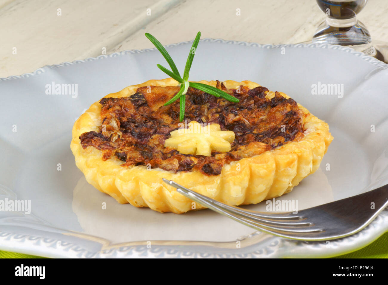 Mini quiche with trevisano chicory on a grey plate and a glass of red wine over a white wooden background Stock Photo