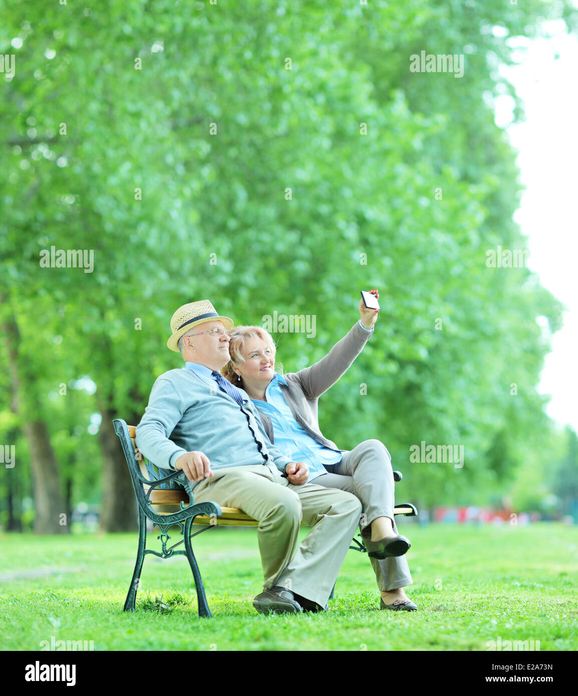Elderly couple taking a selfie in the park seated on a wooden bench Stock Photo