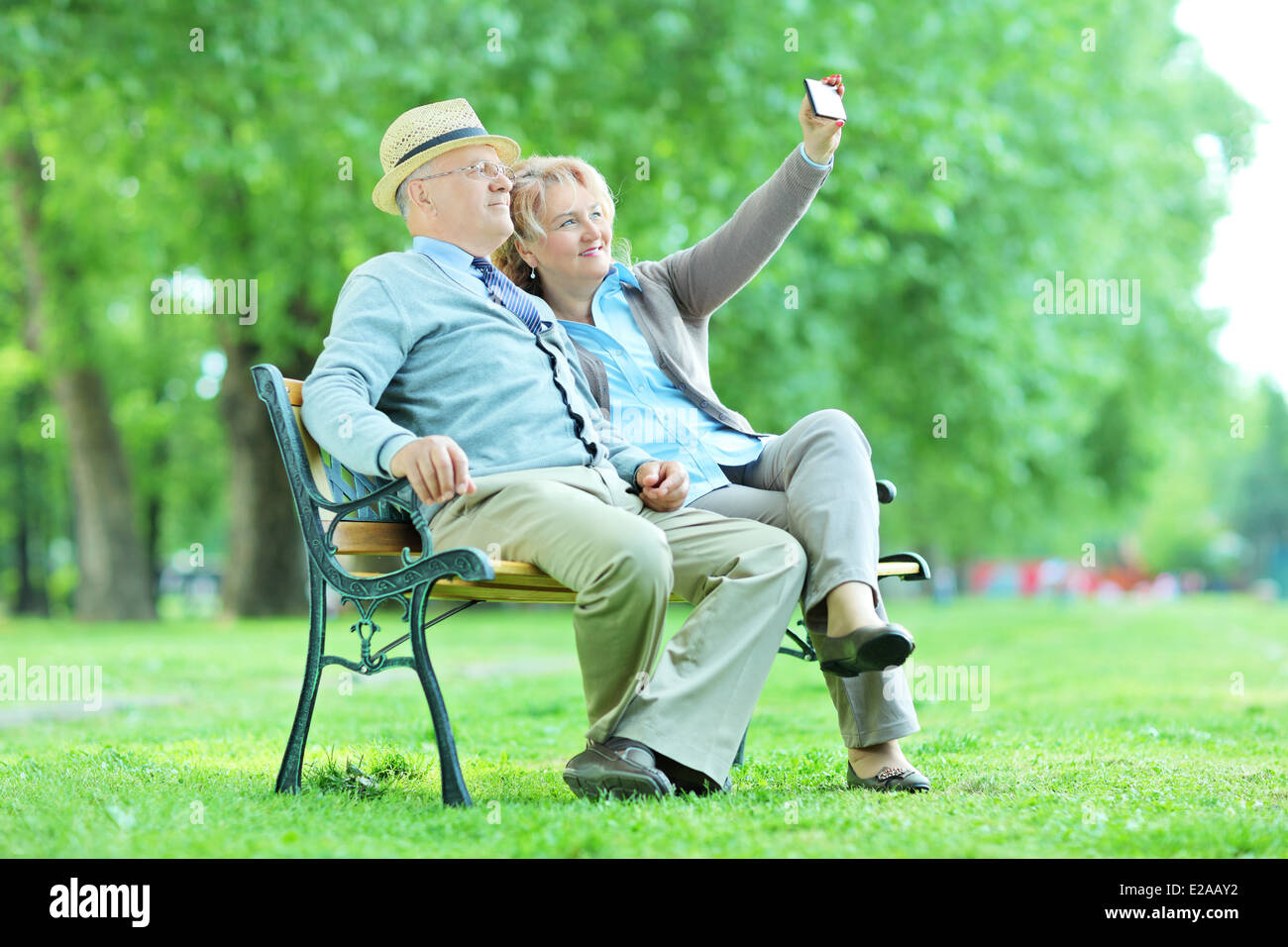Mature husband and wife taking selfies in the park seated on a wooden bench Stock Photo