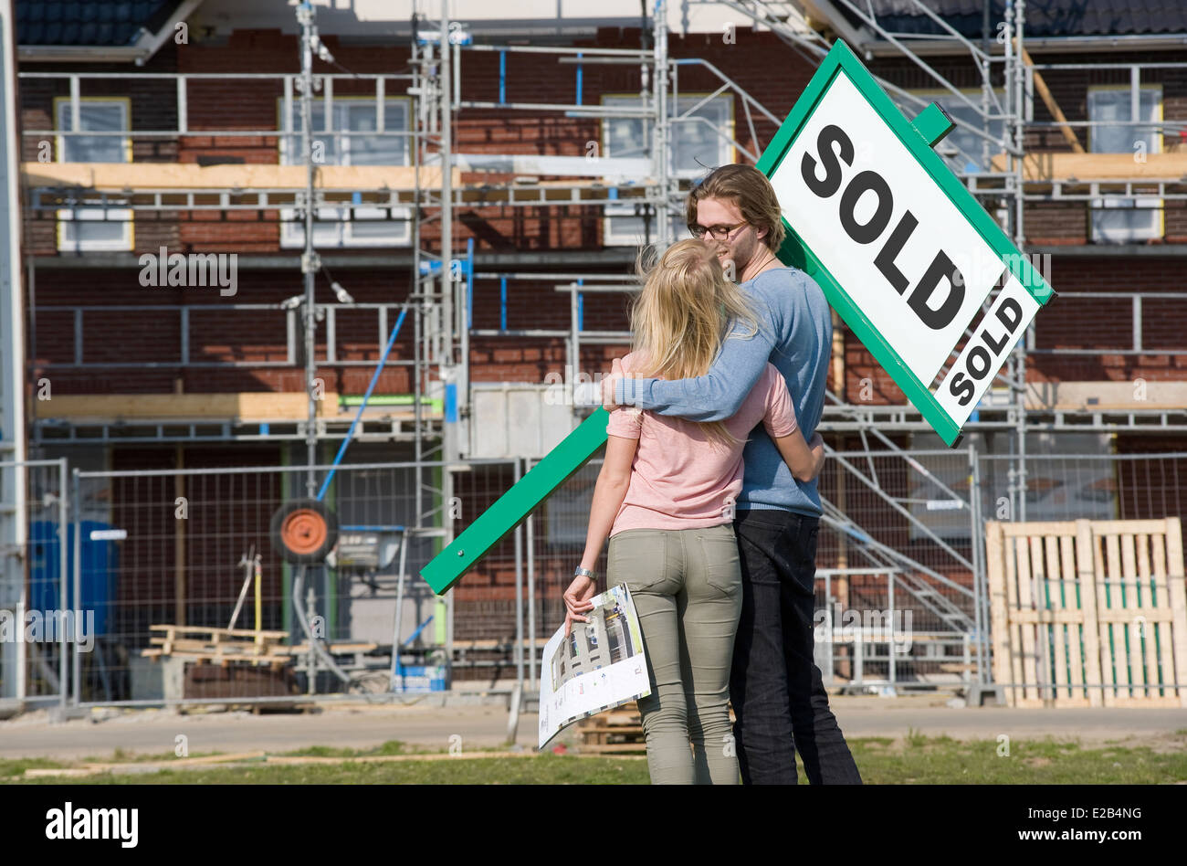 Young couple with blueprint is happy in front of their new built house they just bought, Stock Photo