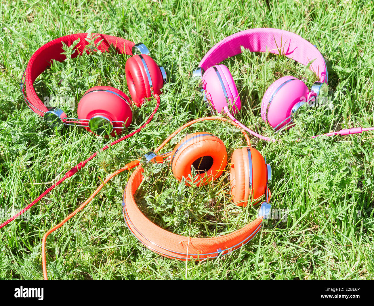Set of three varicolored colorful headphones on sunlight fresh green sward Stock Photo