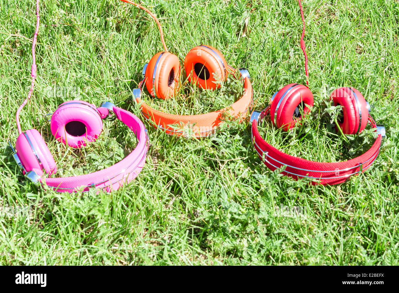 Multicolored kit for mobile mp3 audio entertainment of three vivid colored headphones on summer sunny glade Stock Photo
