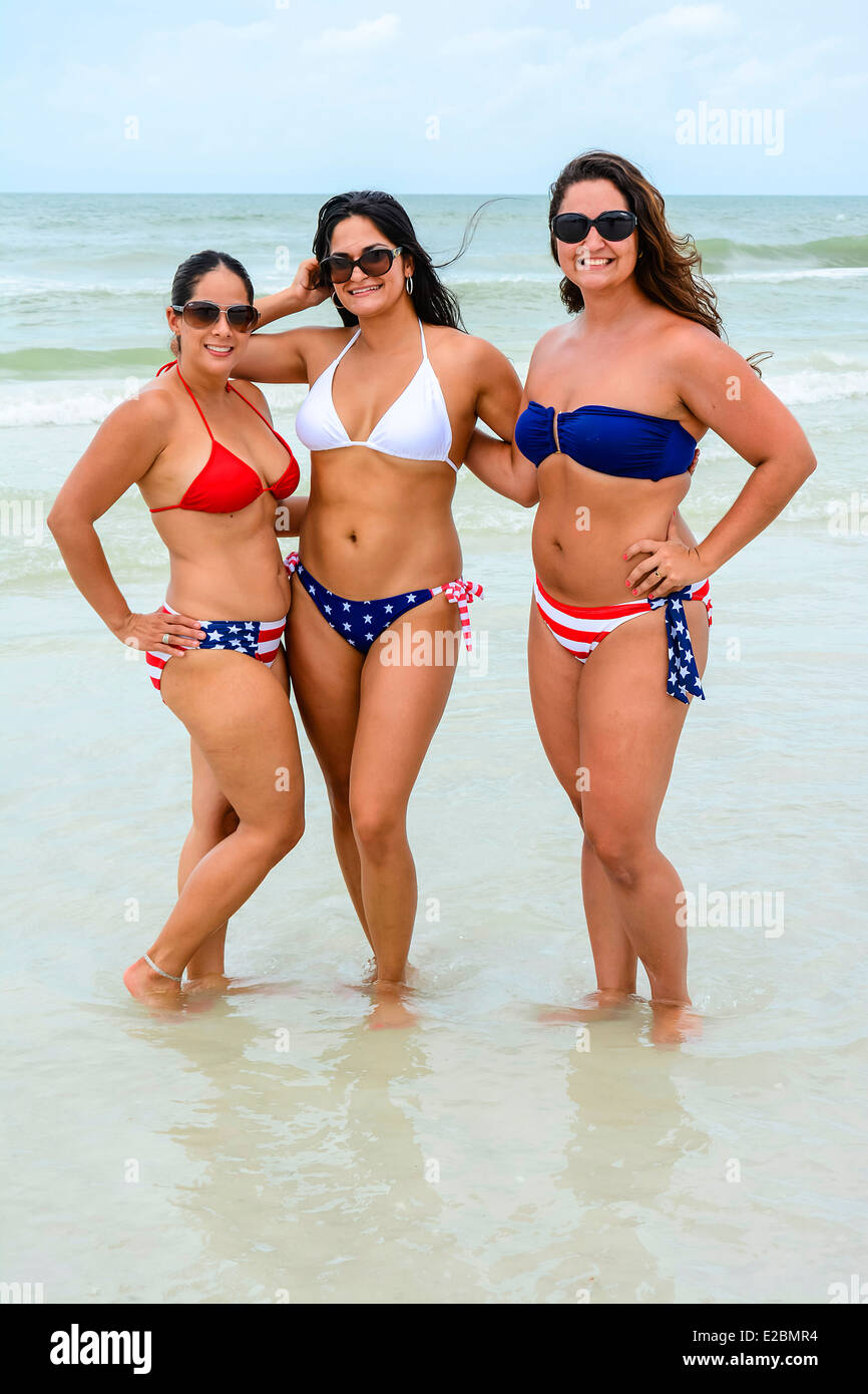 Three patriotic women pose in the surf at the beach on the Fourth of July in their red, white & blue bikinis Stock Photo