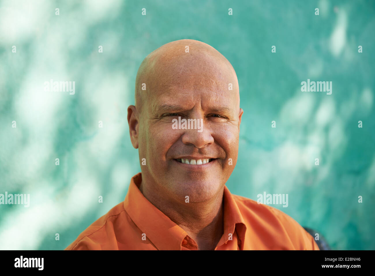 Portrait of mature caucasian man with orange shirt sitting in park and looking at camera with happy expression Stock Photo
