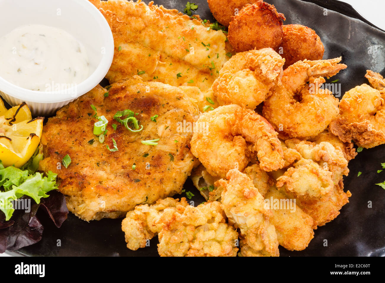 Fried seafood platter with fish, shrimp, oysters, hush puppies, and a crab cake. Stock Photo