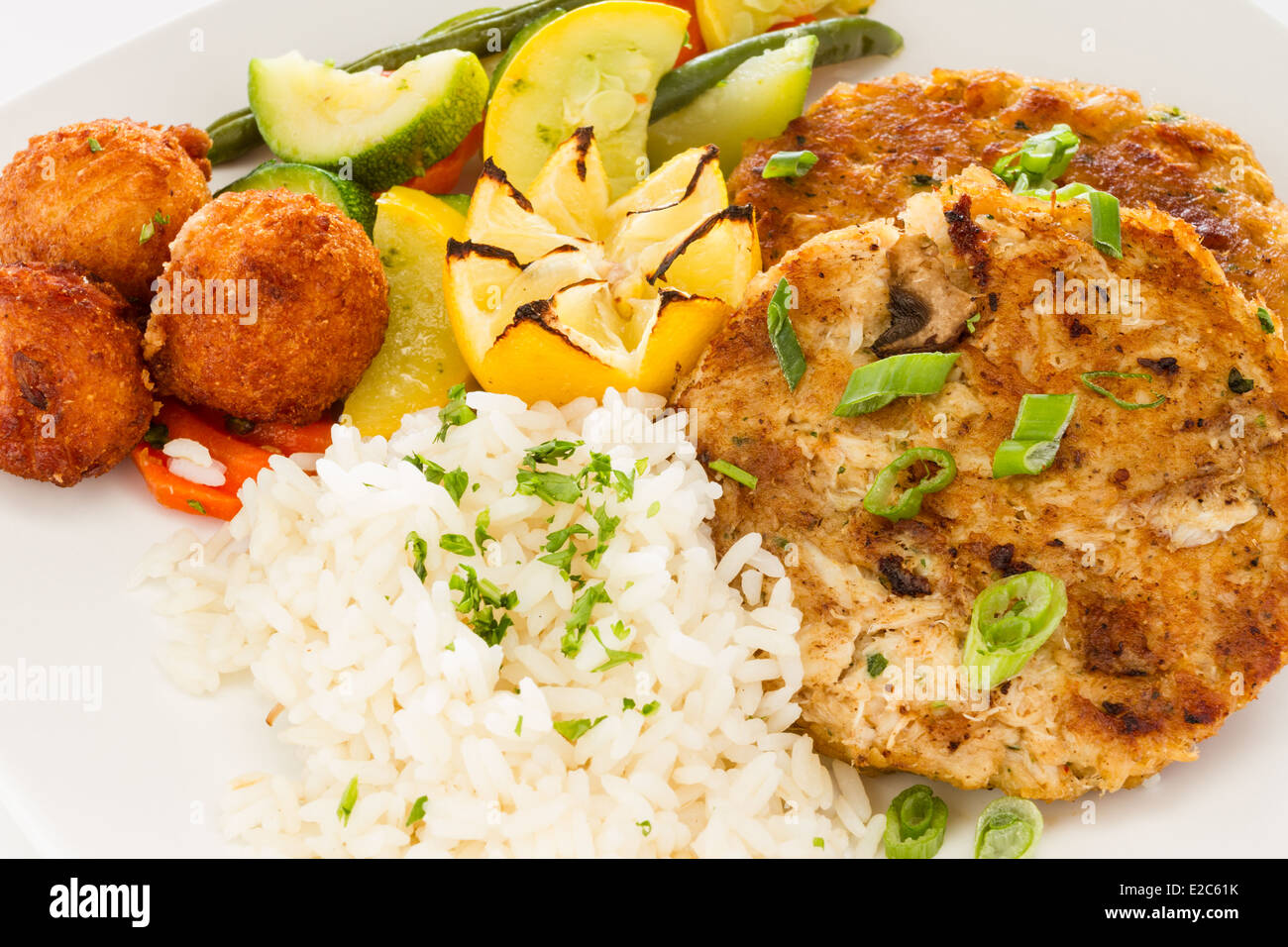Pan fried crab cake sandwich served with a side of rice, vegetable medley and hush puppies. Stock Photo