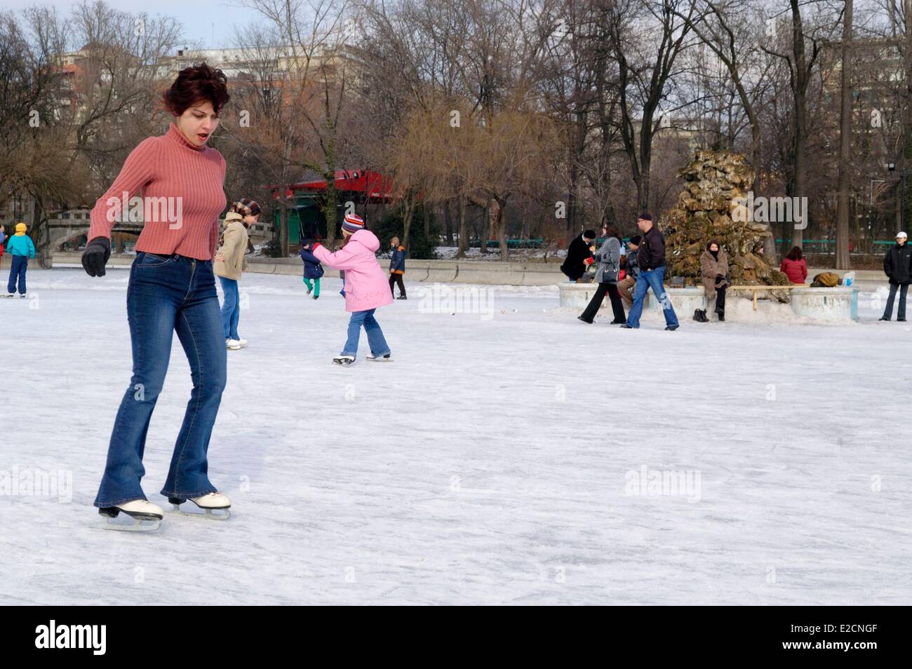 Romania Muntenia Bucharest lake and park Cismigiu natural ice rink young woman in red pull over skating on the frozen lake Stock Photo