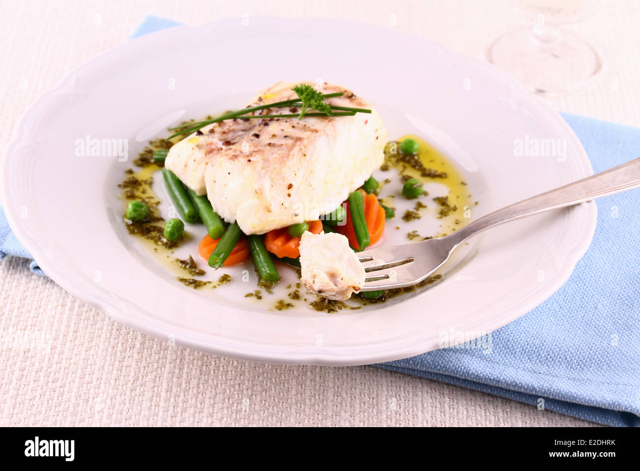 Cod fillet on fork with green beans, peas, parsley, olive oil, close up Stock Photo