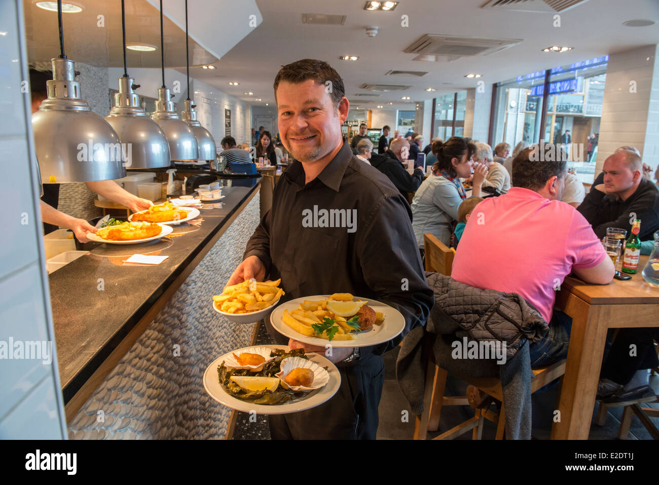 Waiter holding plates of food from Rick Stein's Fish & Chips restaurant and take away. Falmouth, Cornwall Stock Photo