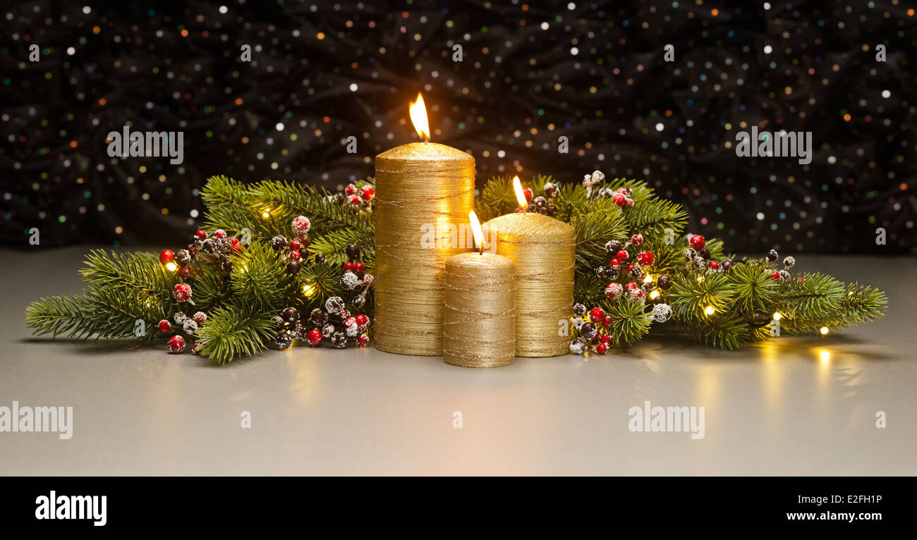 Three golden Candles with Christmas tree branches and red berries decorated Stock Photo