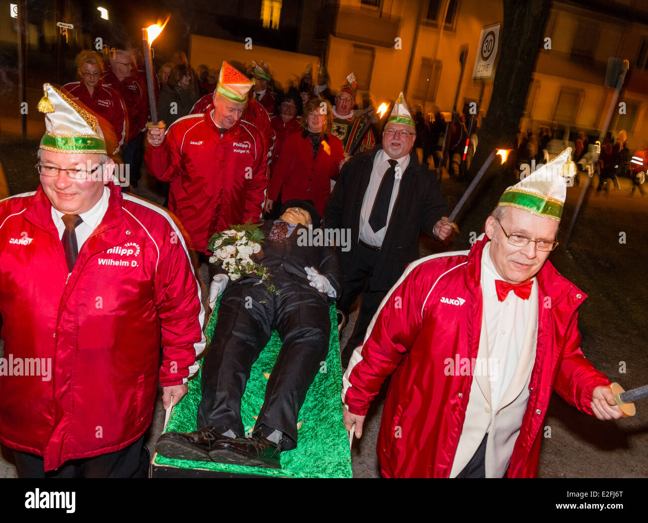 German carnival revelers in good mood carry the deceased Bacchus dummy to his cremation burial with a torchlight procession. Stock Photo
