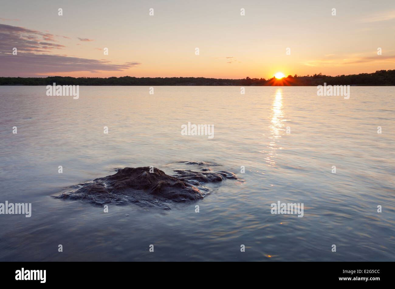The setting sun over a rock that barely sits above the water in Georgian Bay. Massasauga PP, Ontario, Canada. Stock Photo