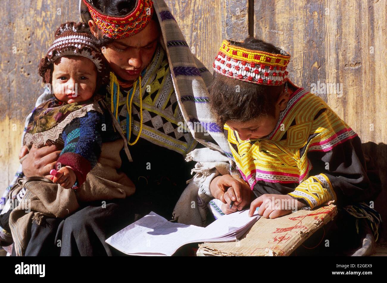 Pakistan Khyber Pakhtunkhwa Kalash valleys Bumburet valley little girl doing her school duties to helped of her mother with little brother on lap in deepest winter end of December to end of February Kalash schools are closed but children have homework to Stock Photo