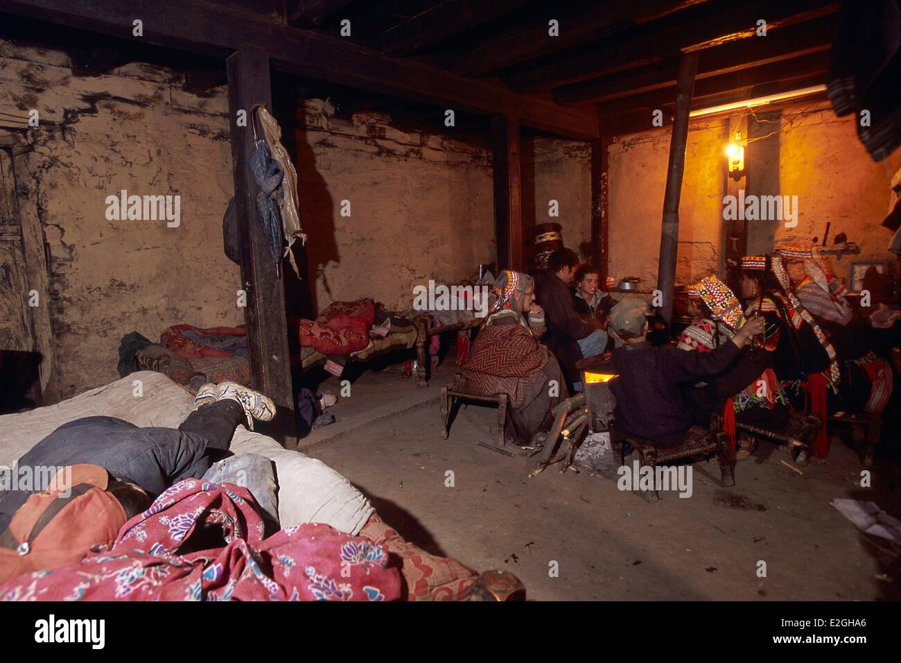 Pakistan Khyber Pakhtunkhwa Kalash valleys Bumburet valley children sleeping on beds that surround single room of Kalash houses while rest of family is seat around stove earthen floor wood stone and wattle and daub walls Stock Photo