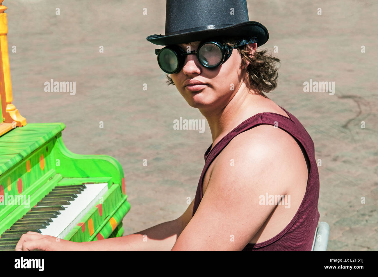Young man in a top hat and goggles playing a colorful piano outdoors. Stock Photo