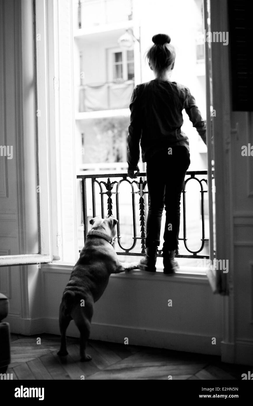 Girl standing on windowsill with pet dog, both looking out Stock Photo
