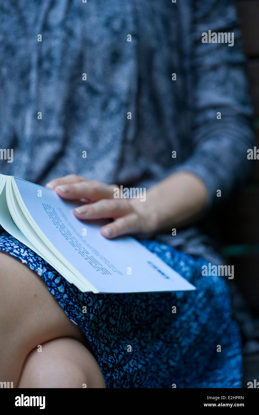 Woman sitting with open book resting on lap, cropped Stock Photo