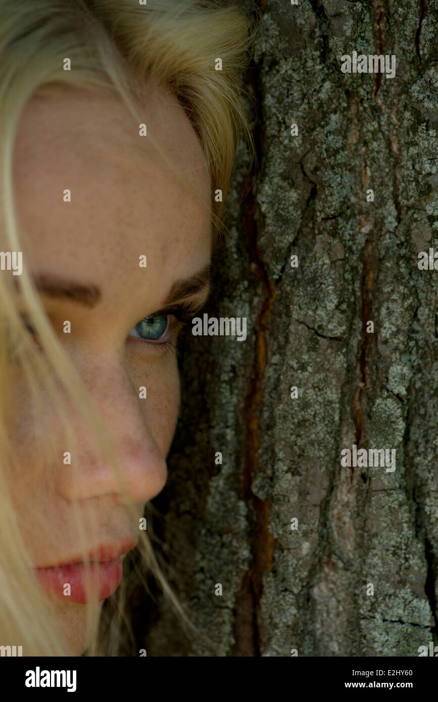 Young Woman Leaning Against Tree Trunk Looking Away Sadly Stock Photo young-woman-leaning-against-tree-trunk-looking-away-sadly-stock-photo