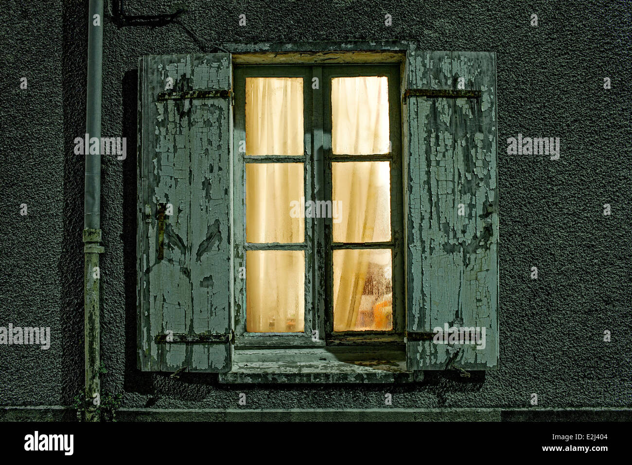 Window with dilapidated shutters illuminated at night Stock Photo