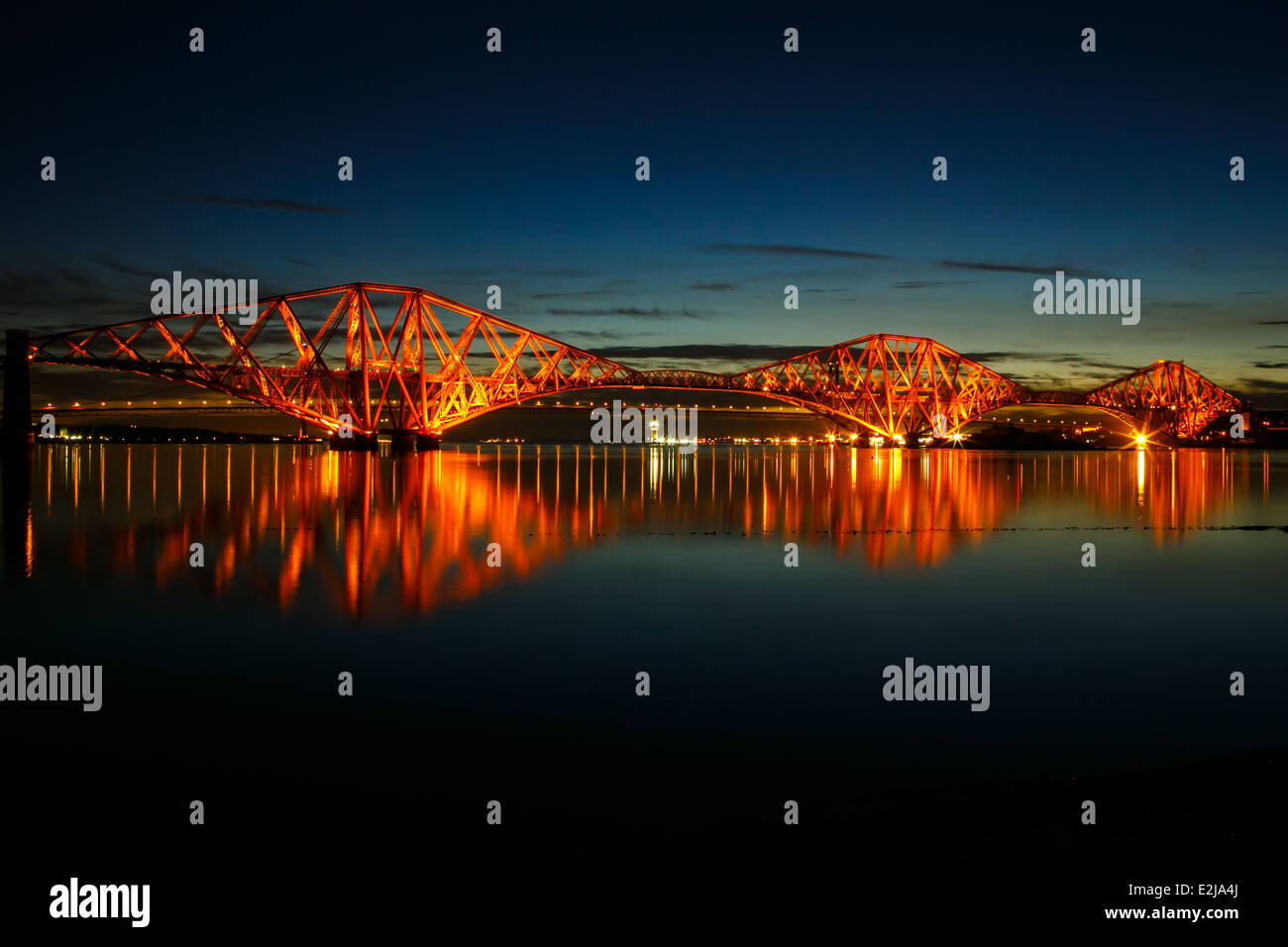 Scotland's Forth Rail Bridge lit up on a spring night with a calm sea. Stock Photo