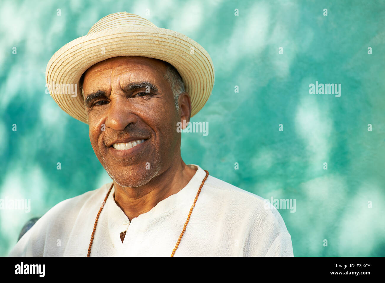 Portrait of retired senior hispanic man with straw hat sitting in park and looking at camera with happy expression Stock Photo