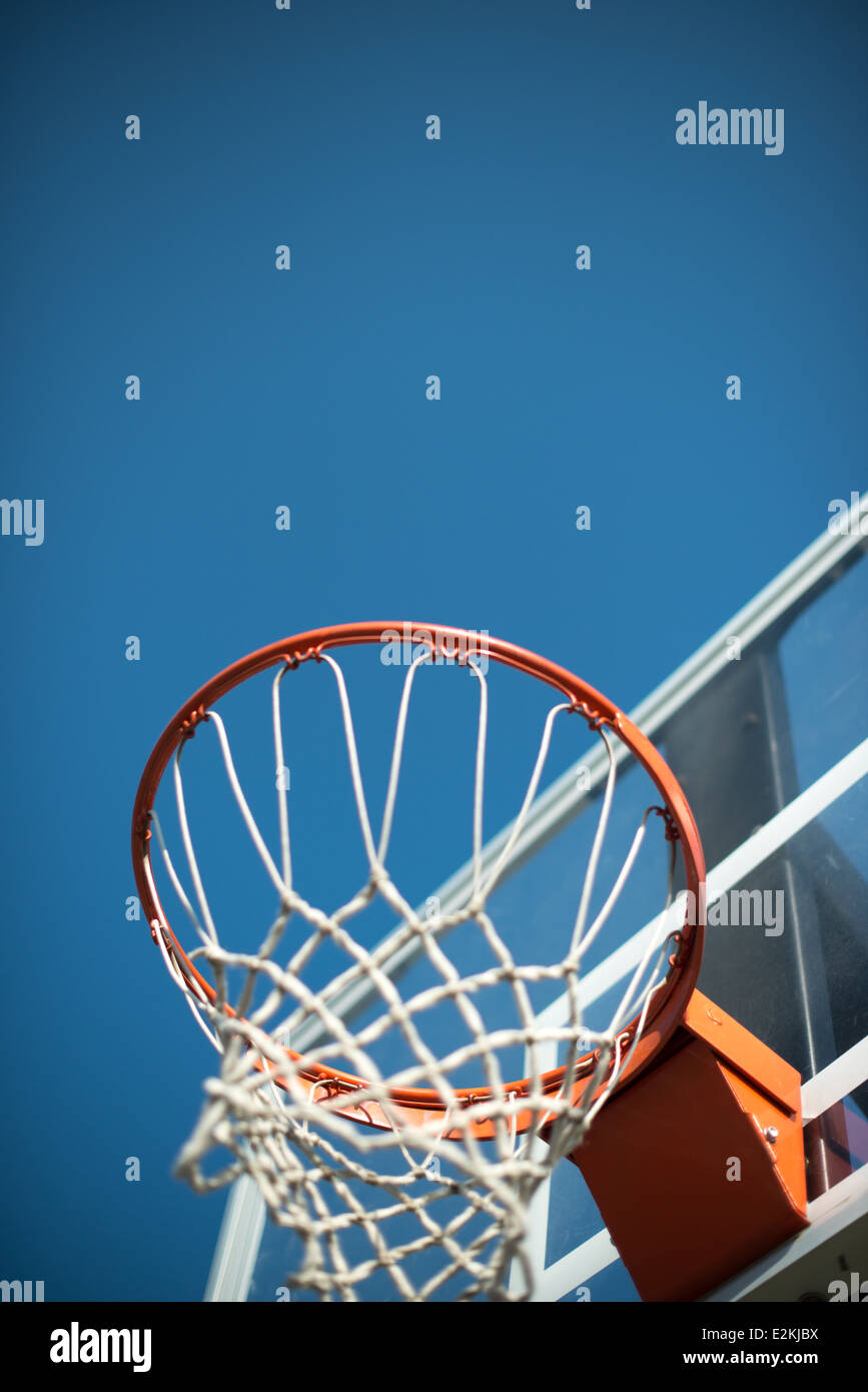 An orange basketball hoop with a transparent backboard with net against a clear blue sky. Stock Photo