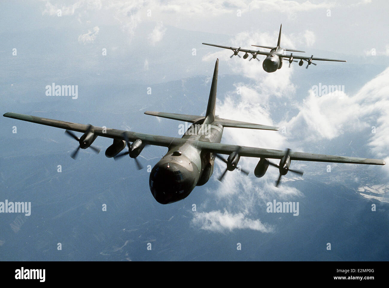 Two C-130E Hercules aircraft flying over mountainous terrain. Stock Photo