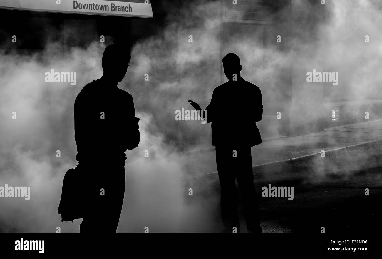 A silhouette of two people standing in the fog outside a downtown bank. Stock Photo