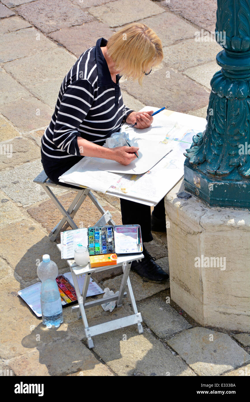 Woman artist painting whilst sitting beside the Giudecca Canal waterfront in Giudecca Canal Venetian Lagoon Venice Italy Stock Photo