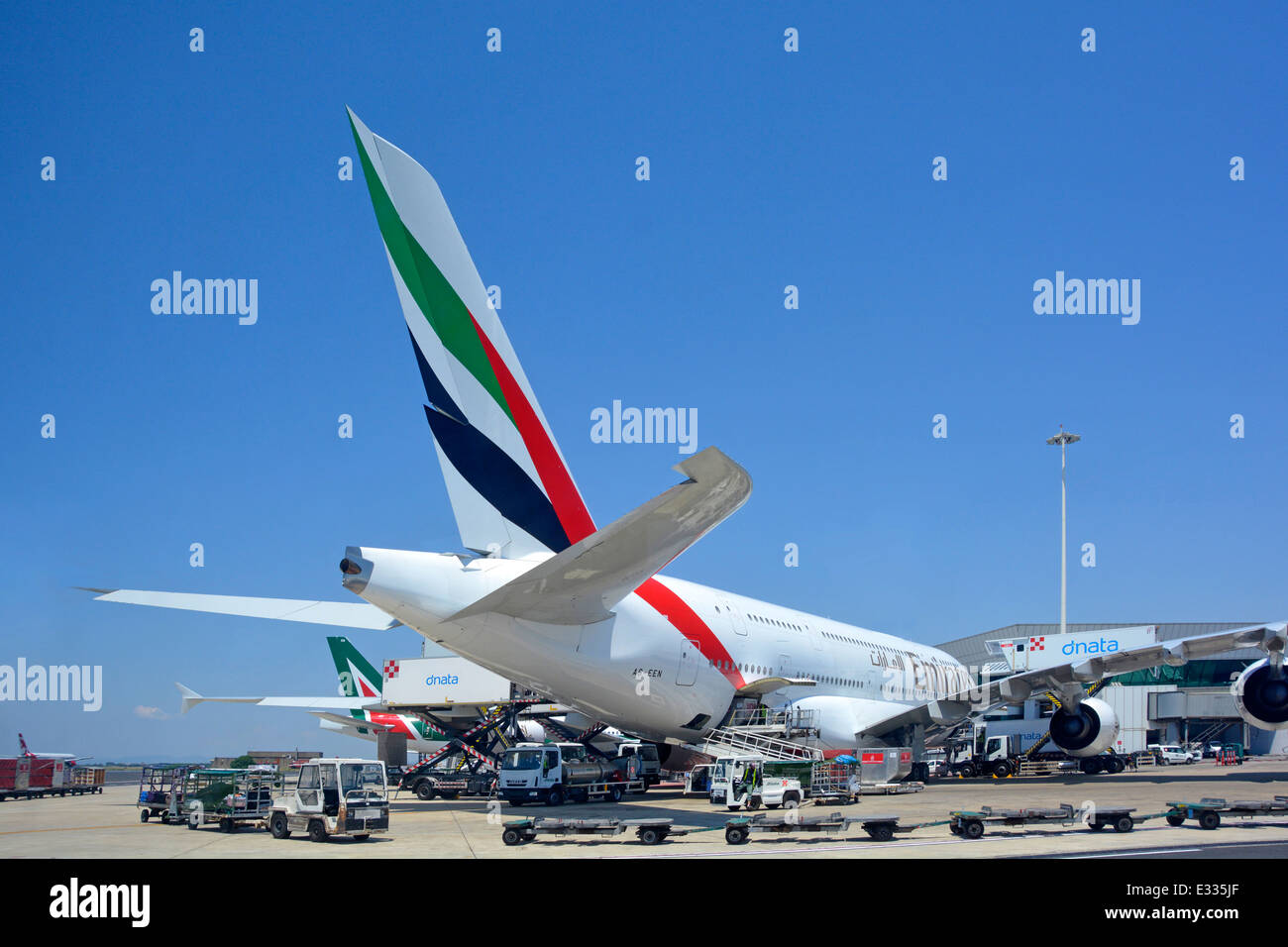 Emirates Airbus A380 double deck wide body four engine jet airplane tail fin logo view at Rome Fiumicino Italy airport apron stand ground crew attend Stock Photo