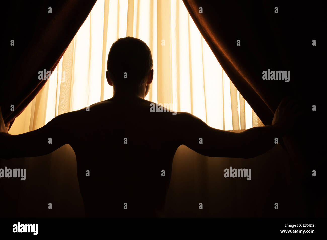 Man in dark room opens curtains on window to the morning sunlight Stock Photo