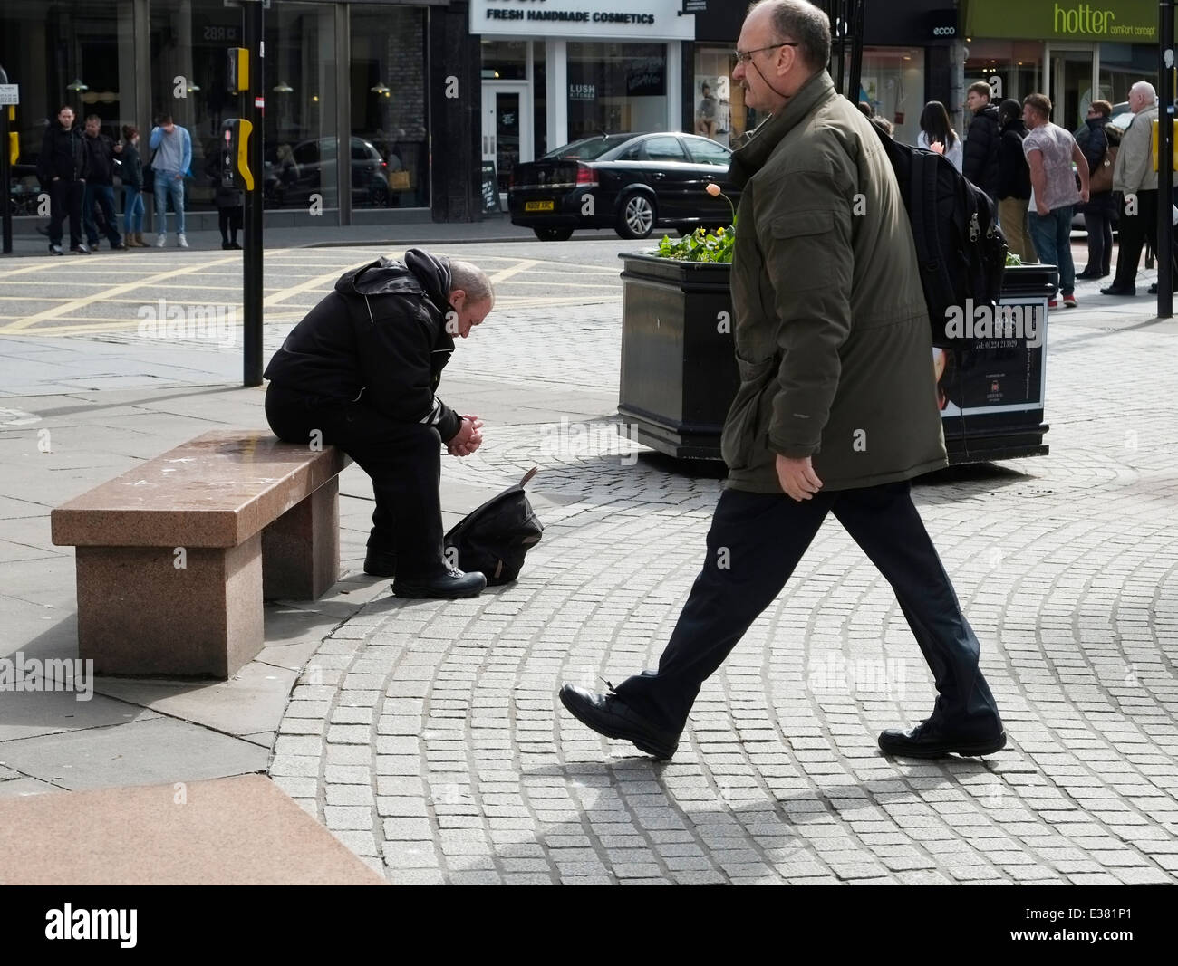 A man sits on a bench in Union Street, Aberdeen. Another man passes by. Stock Photo