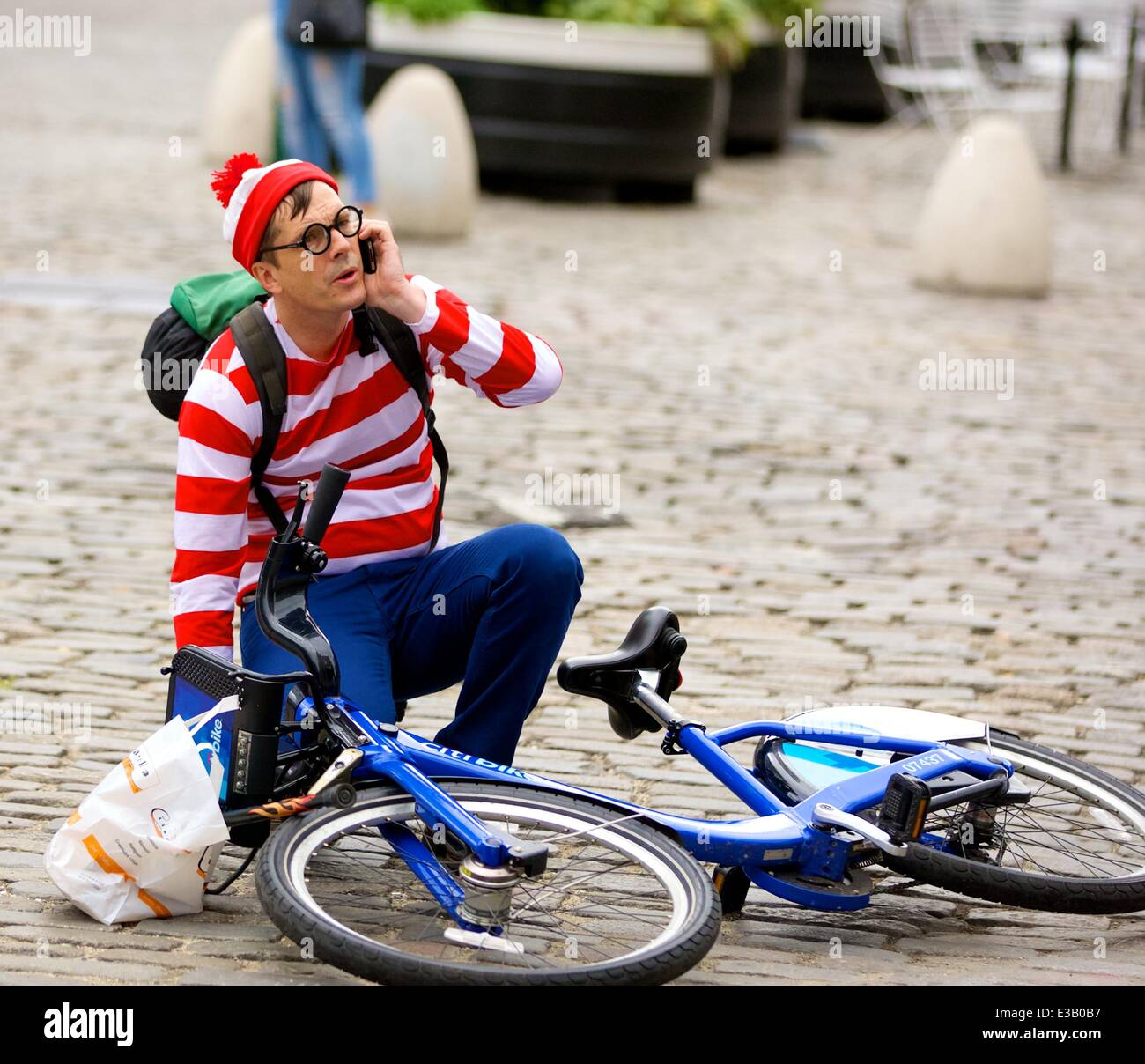 A man dressed as the character Waldo from the children's book series, 'Where's Waldo?' is spotted riding a Citi Bike in the Meatpacking District. With his hands full, Waldo eventually falls off his bicycle to the ground  Featuring: Waldo,Wally Where: New York City, NY, United States When: 14 Sep 2013 Stock Photo