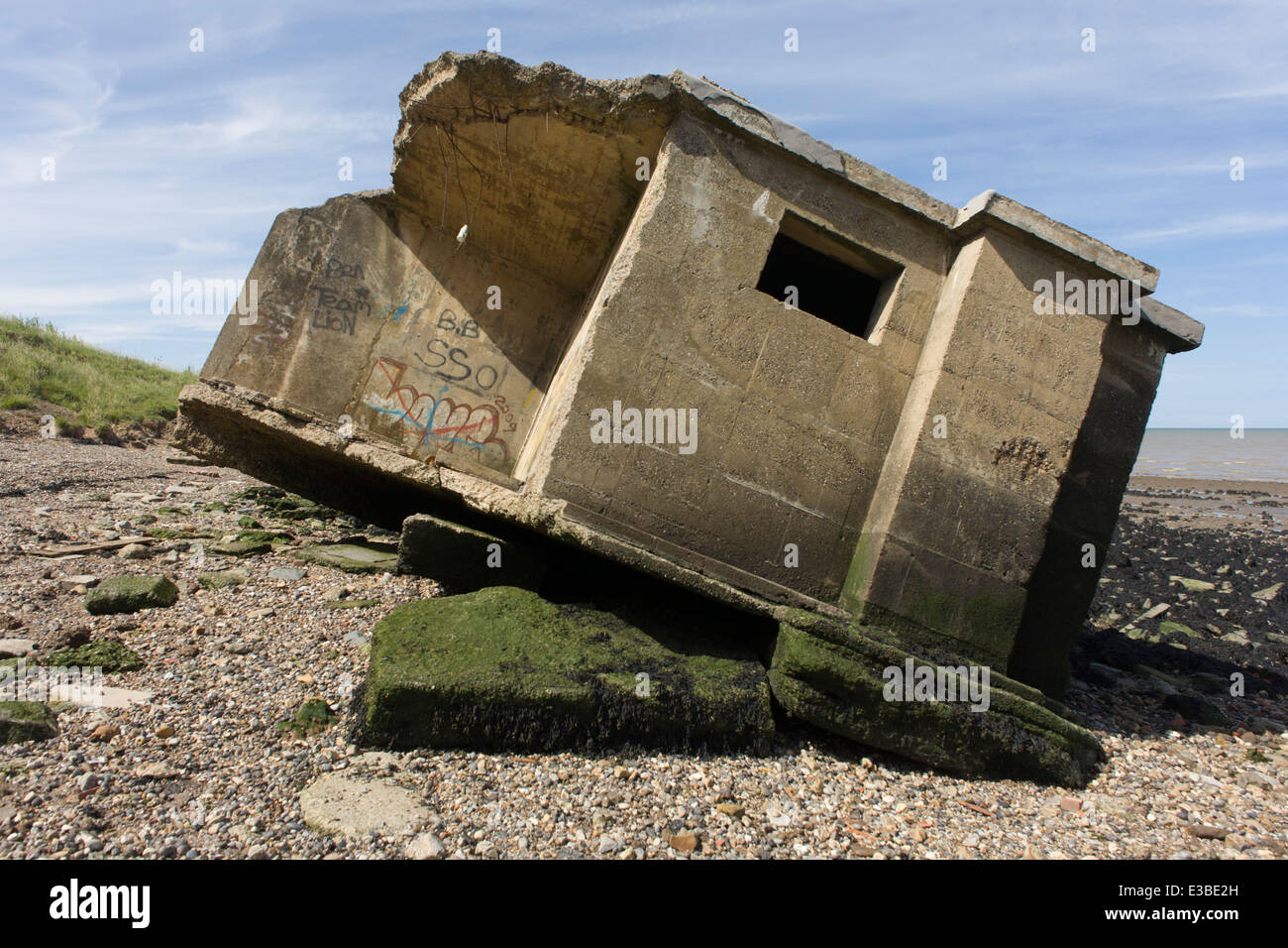 WW2-era concrete pillbox defence structure lies on the beach after coastal erosion at Warden Point, Isle of Sheppey, Kent. Stock Photo
