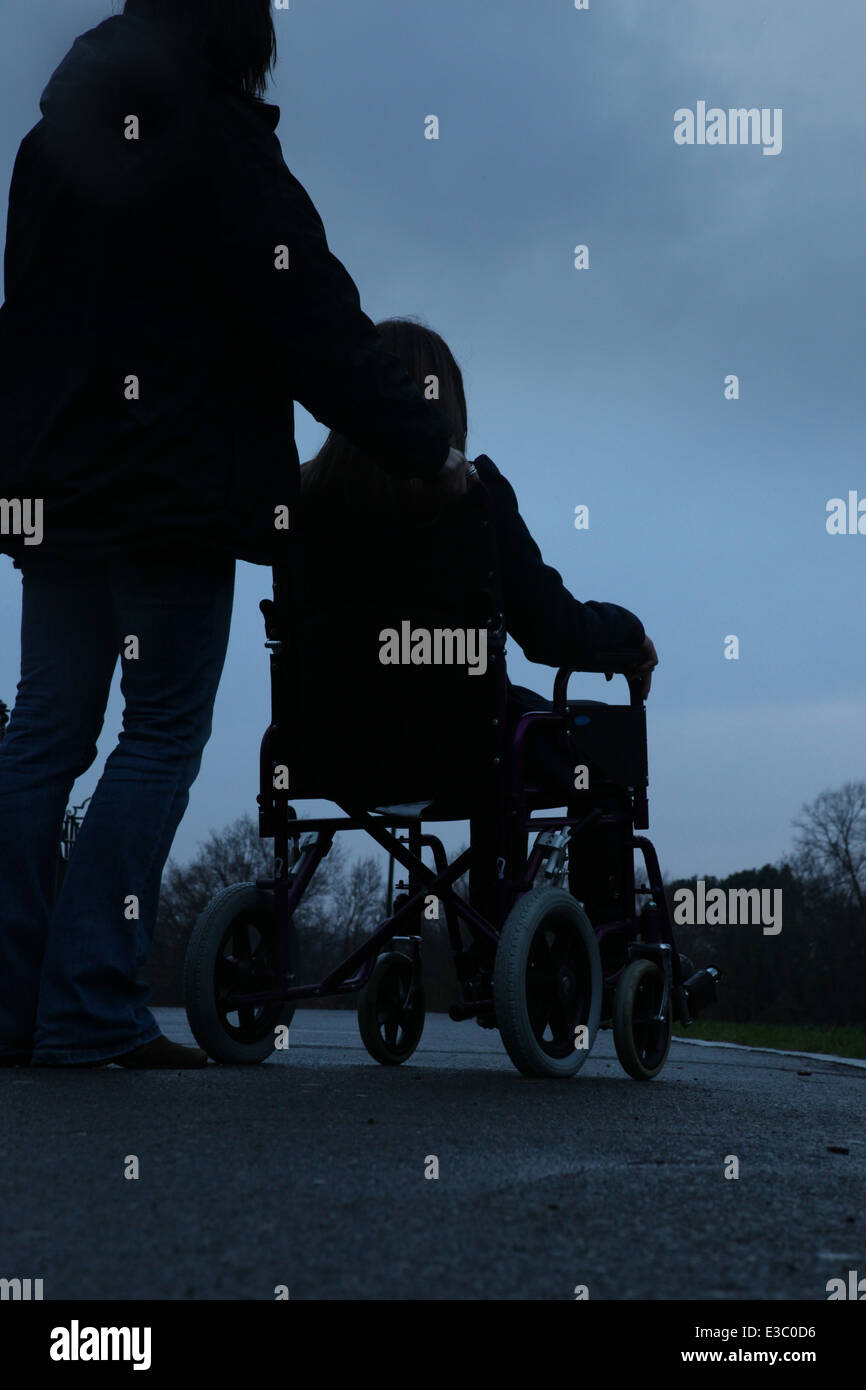 Woman pushing a young girl sitting in a wheelchair. Stock Photo