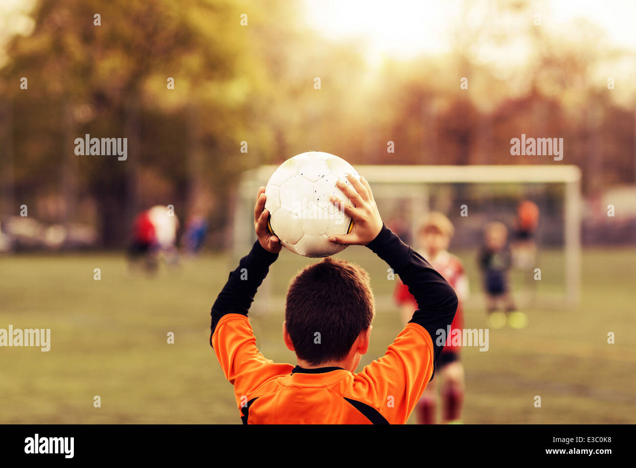 young football player making throw-in with ball in evening sunshine Stock Photo