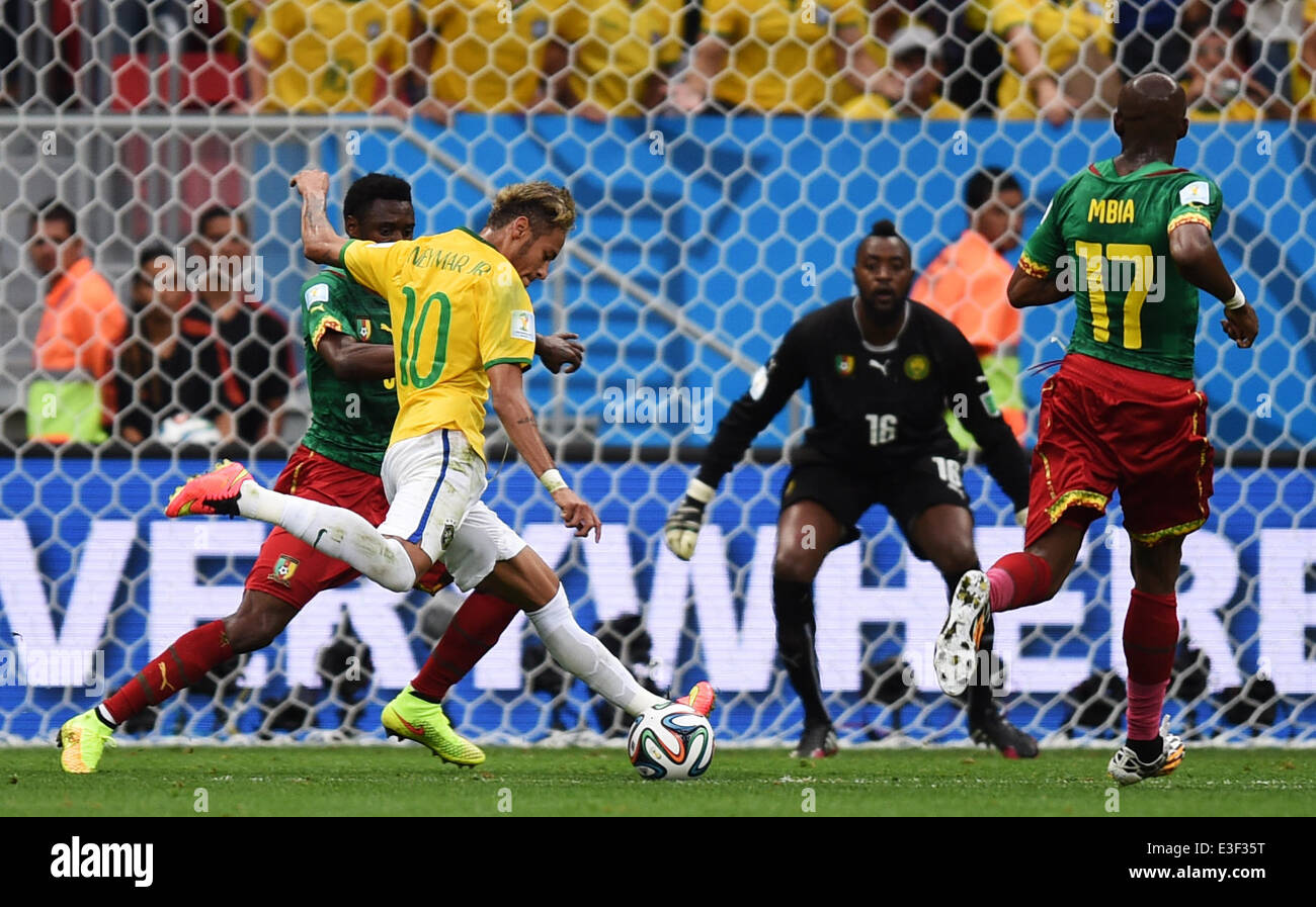 Brasilia, Brazil. 23rd June, 2014. Neymar of Brazil (2-L) takes a shot against Cameroon's Nicolas Nkoulou (L) and goal keeper Charles Itandje (2-R) during the FIFA World Cup 2014 group A preliminary round match between Cameroon and Brazil at the Estadio Nacional in Brasilia, Brazil, 23 June 2014. Photo: Marius Becker/dpa/Alamy Live News Stock Photo